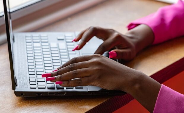 A woman with pink fingernails typing on a laptop.