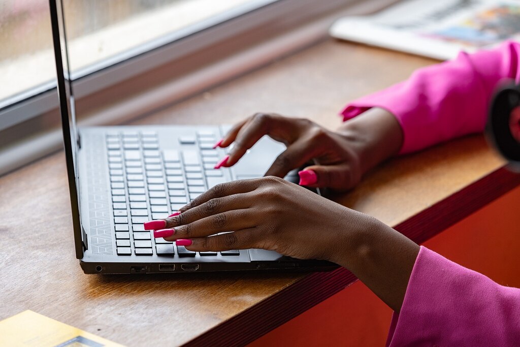 A woman with pink nail polish typing on a laptop.