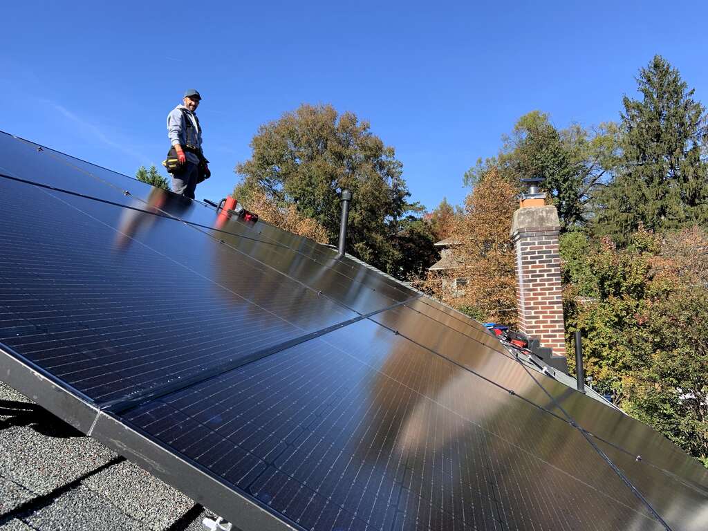Black solar panels on a roof with a solar installer smiling in the background.