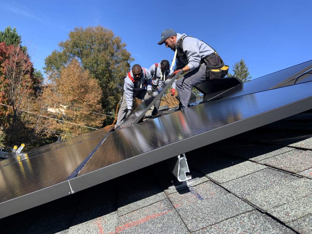 Three solar installers on a roof easing a solar panel into place.