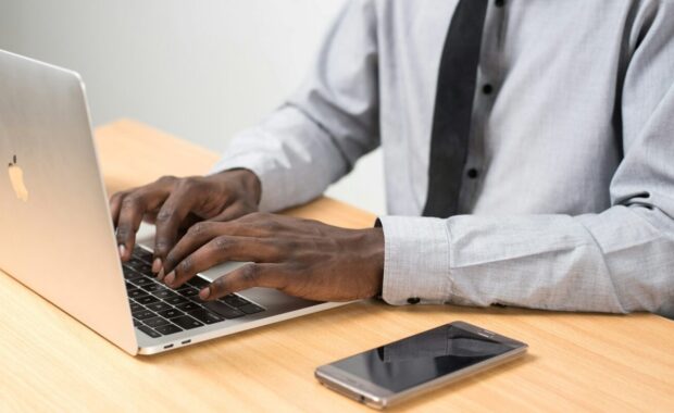 A man in business attire types on a laptop.