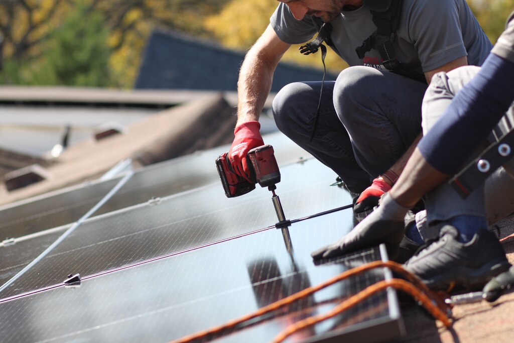 A solar installer bolts a solar panel into place while another installer holds the panel steady.
