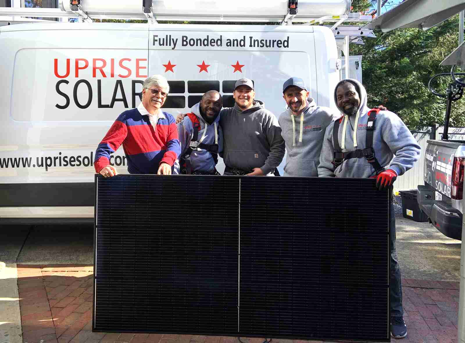 An Uprise customer and four installers posing with a solar panel in front of the Uprise truck.