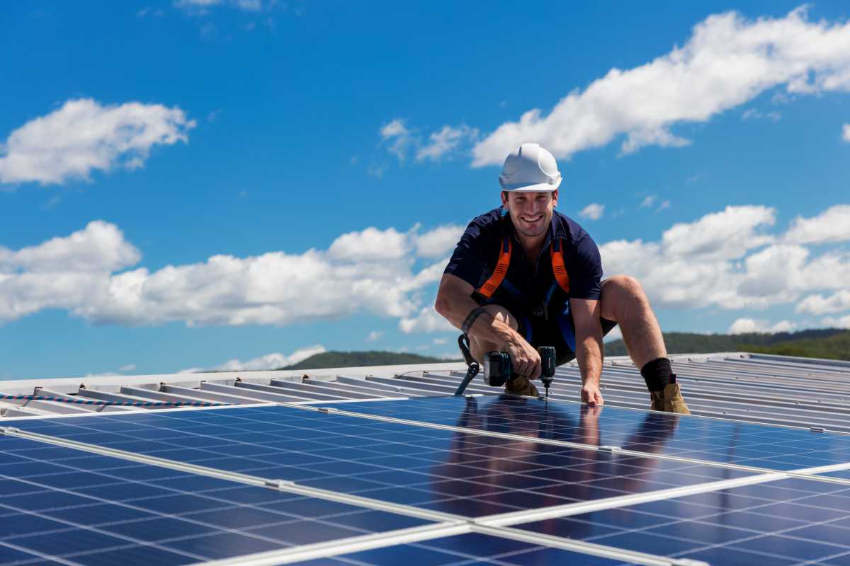solar installer smiling and holding a drill in hand while on roof of a home