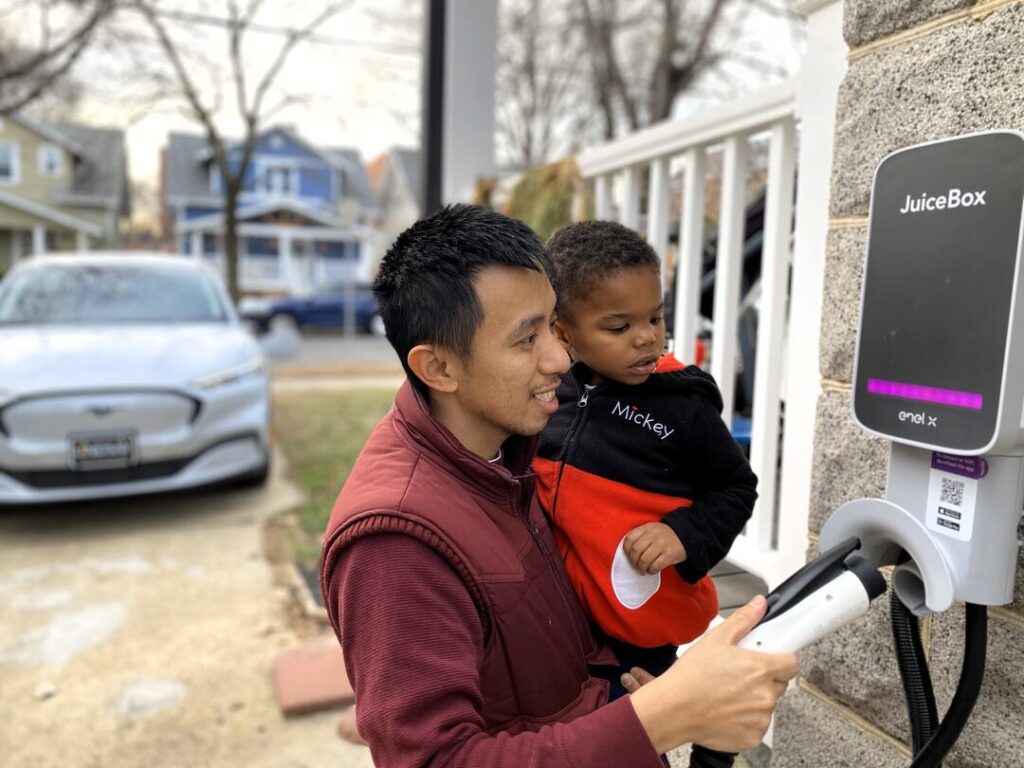 A man and his son plug in an electric car at a home EV charger.