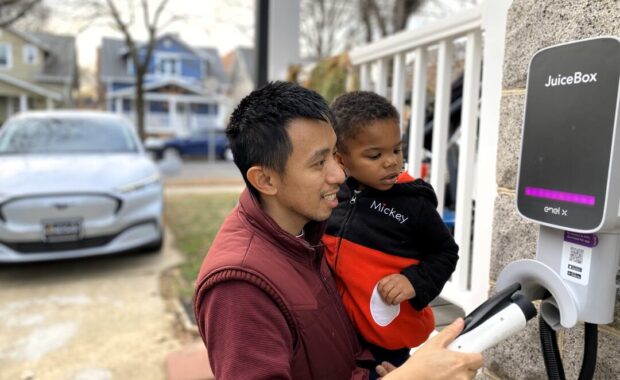 A man and his son plug in an electric car at a home EV charger.