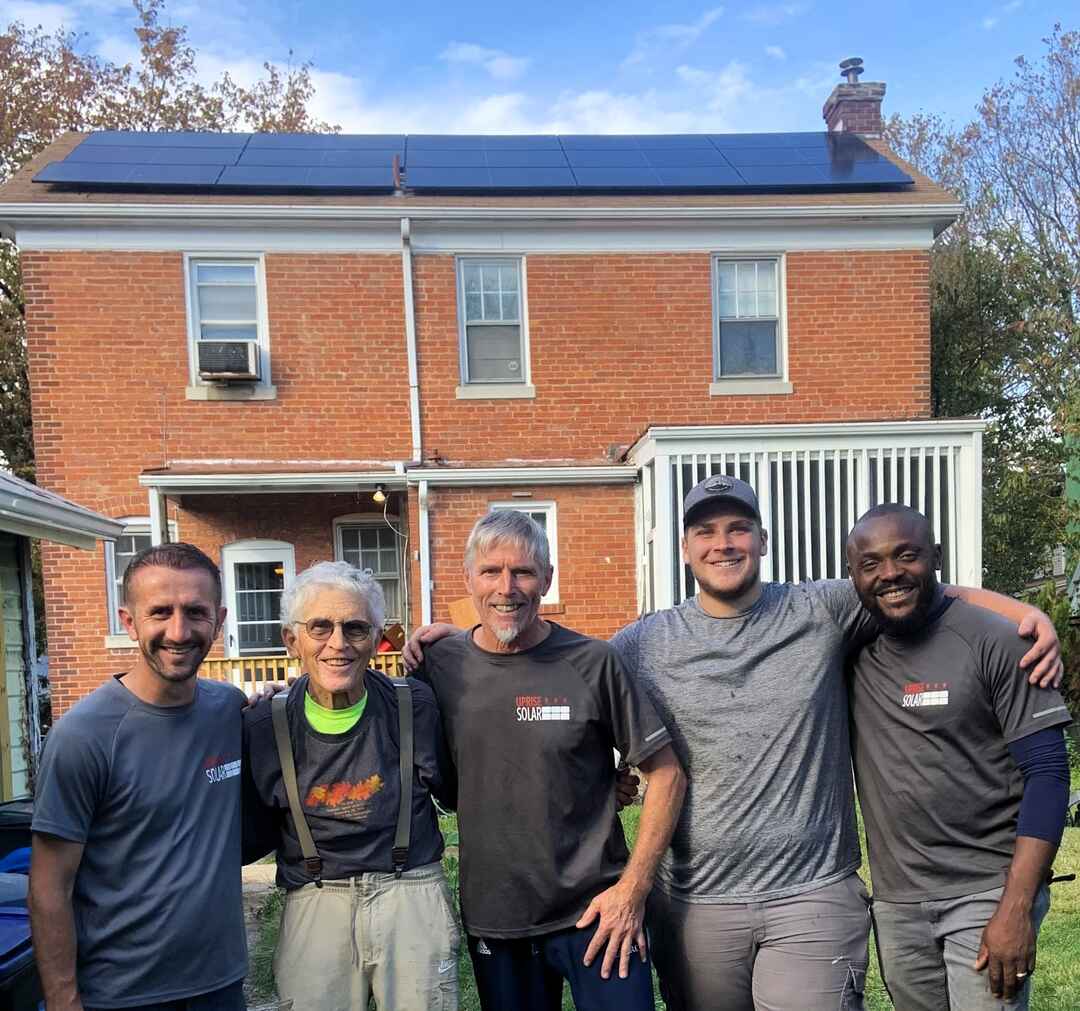 Four Uprise solar installers and a customer stand in front of a home with new solar panels.