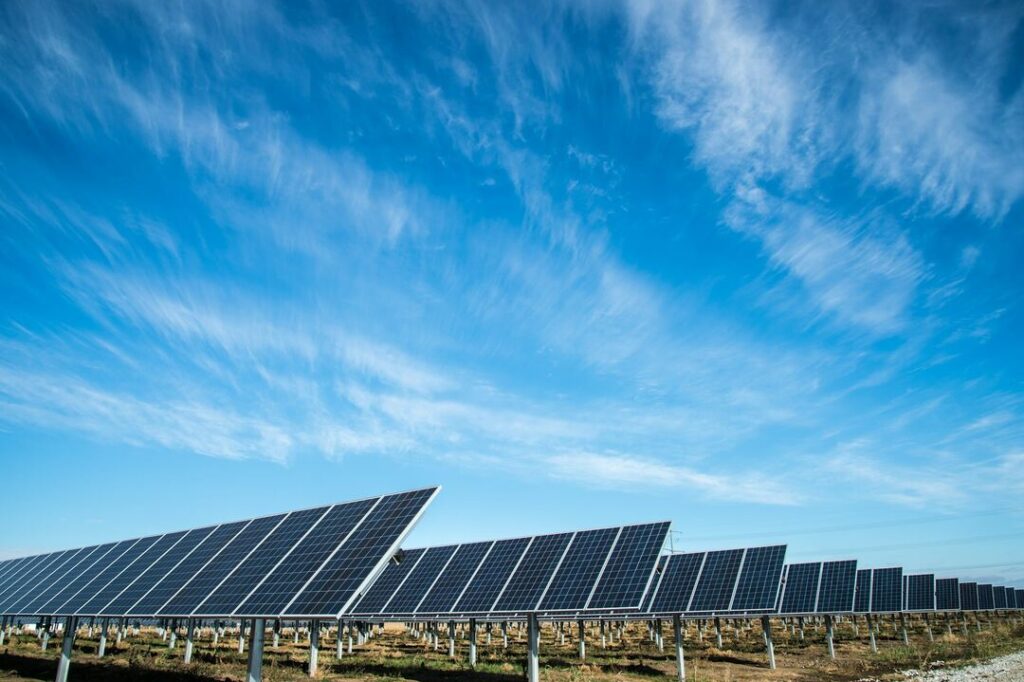 Solar panels under a blue sky with wispy white clouds.