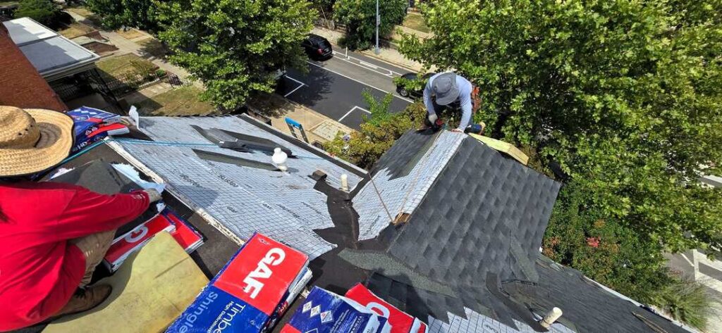 Two roofers work on a shingle roof.