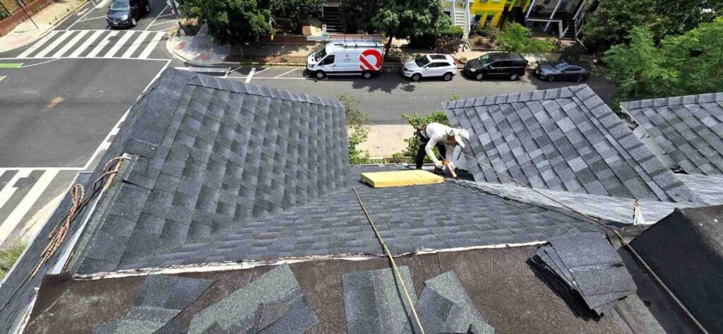 A roofer working on a shingle roof with an Uprise Solar truck in the background.