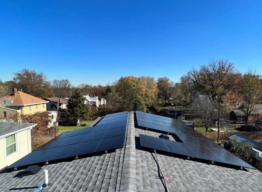 Solar panels on a shingle roof under a bright blue sky.