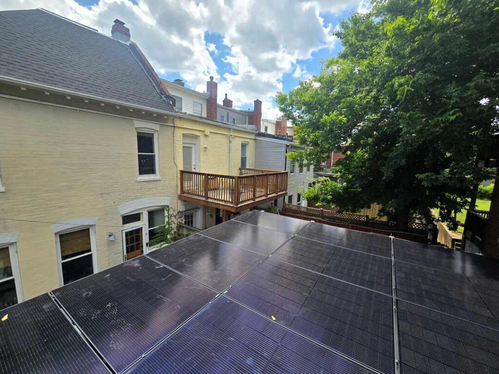 Solar panels on a roof with homes in Northwest Washington, DC in the background.