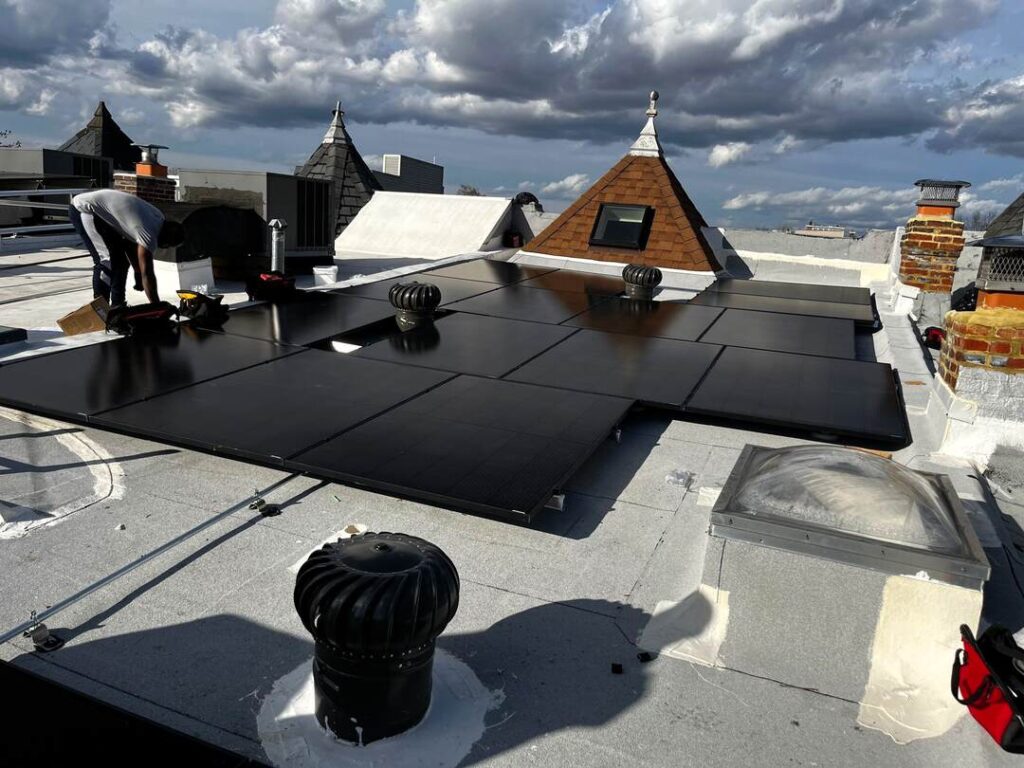 A solar installer works on a solar array with dramatic clouds in the background.