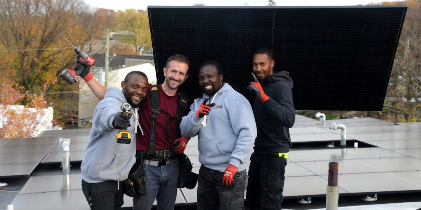 Four solar installers pose with tools and a black solar panel.