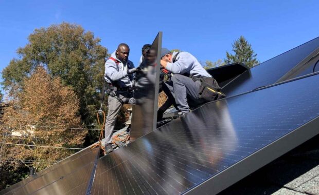 Three solar installers work to put a solar panel in place.