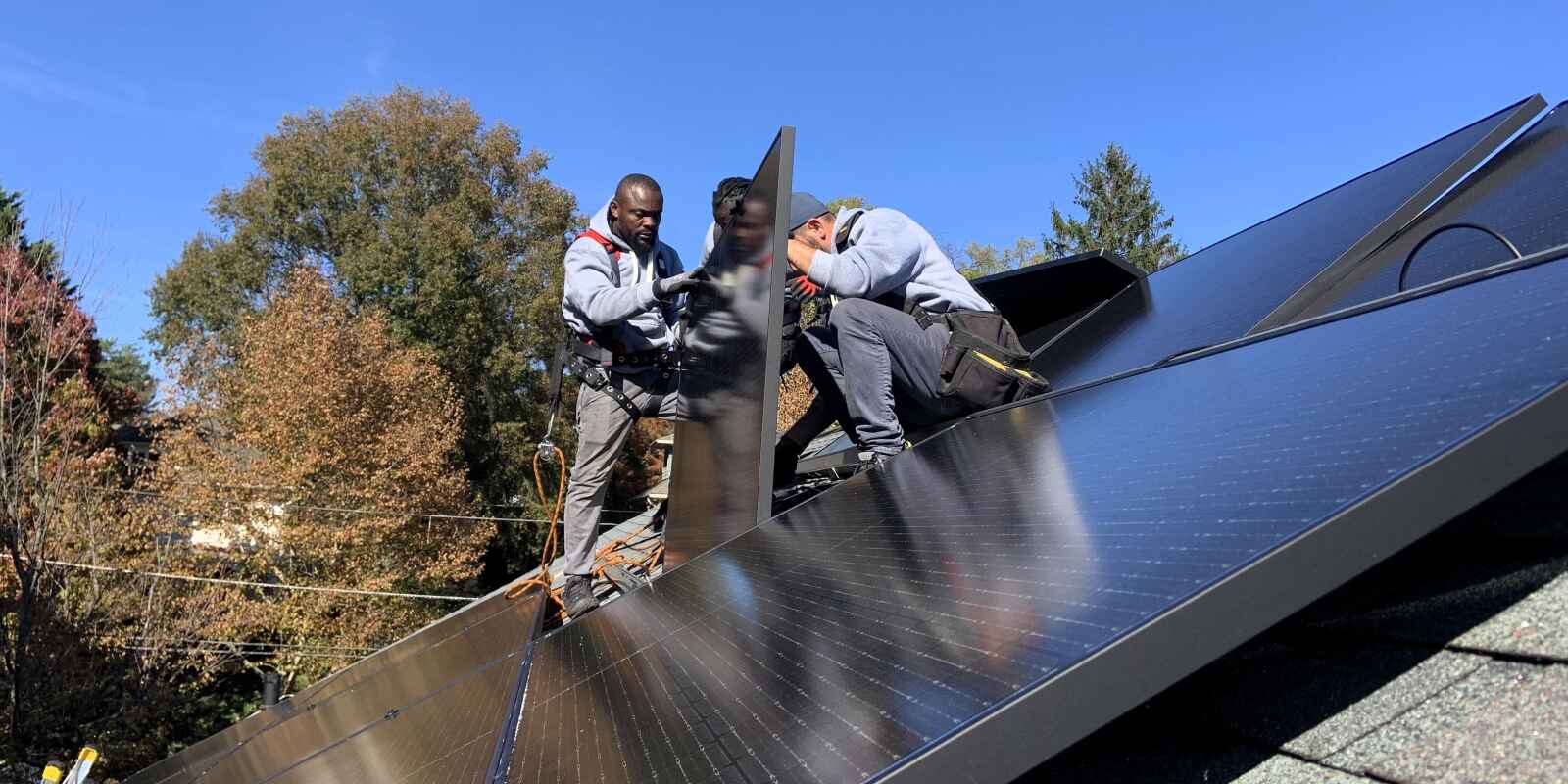 Three solar installers work to put a solar panel in place.