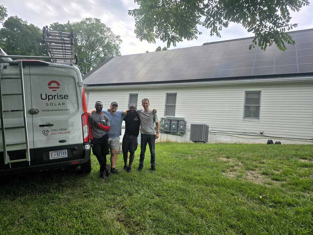 Four members of Uprise Solar's construction team stand next to an Uprise truck in front of a completed solar array.