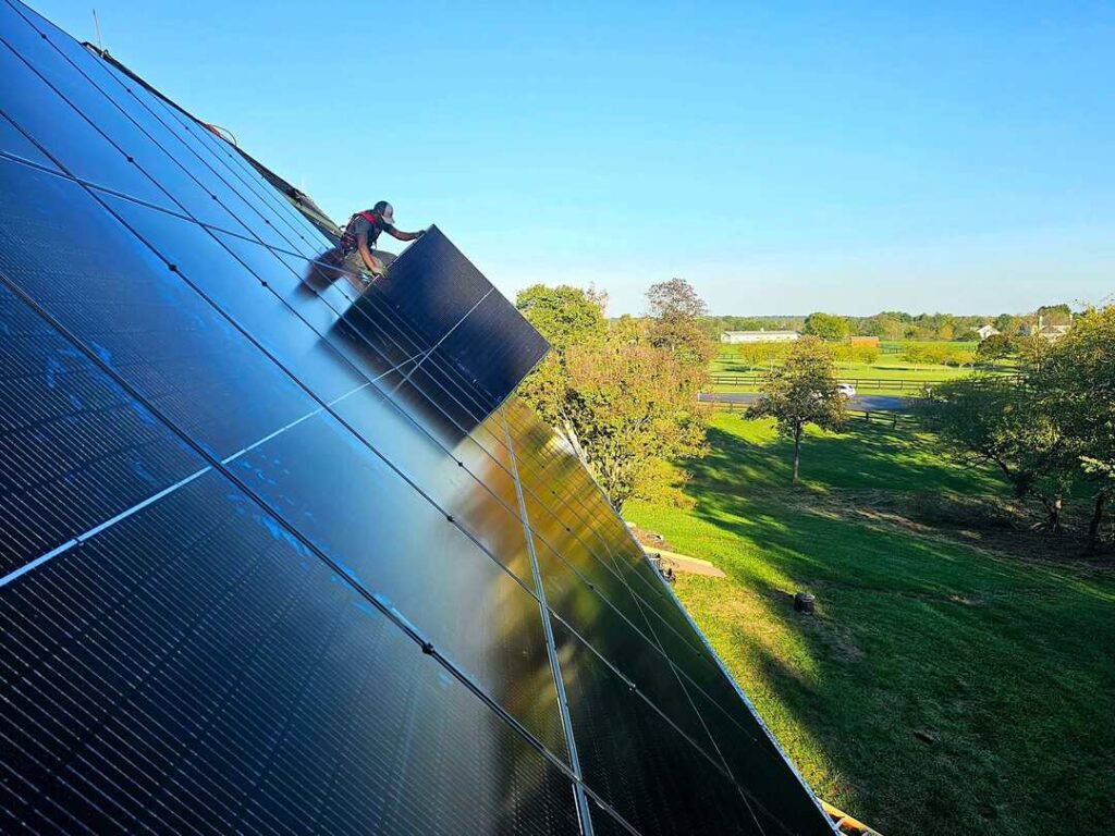 A solar installer on a roof with green fields in Virginia in the background.