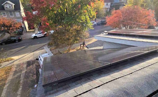 Solar panels on a sloped roof with fall leaves in the background on a residential street.