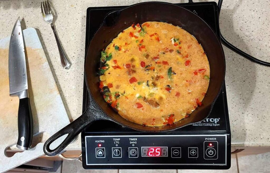 Eggs with salsa, green onions, and sweet peppers in a pan on an induction hot plate.