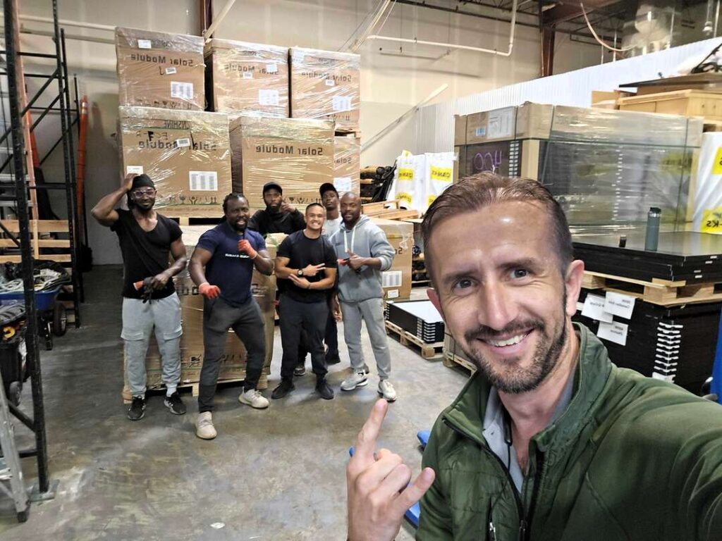 Uprise Solar installers smile in the warehouse with a delivery of new solar panels.