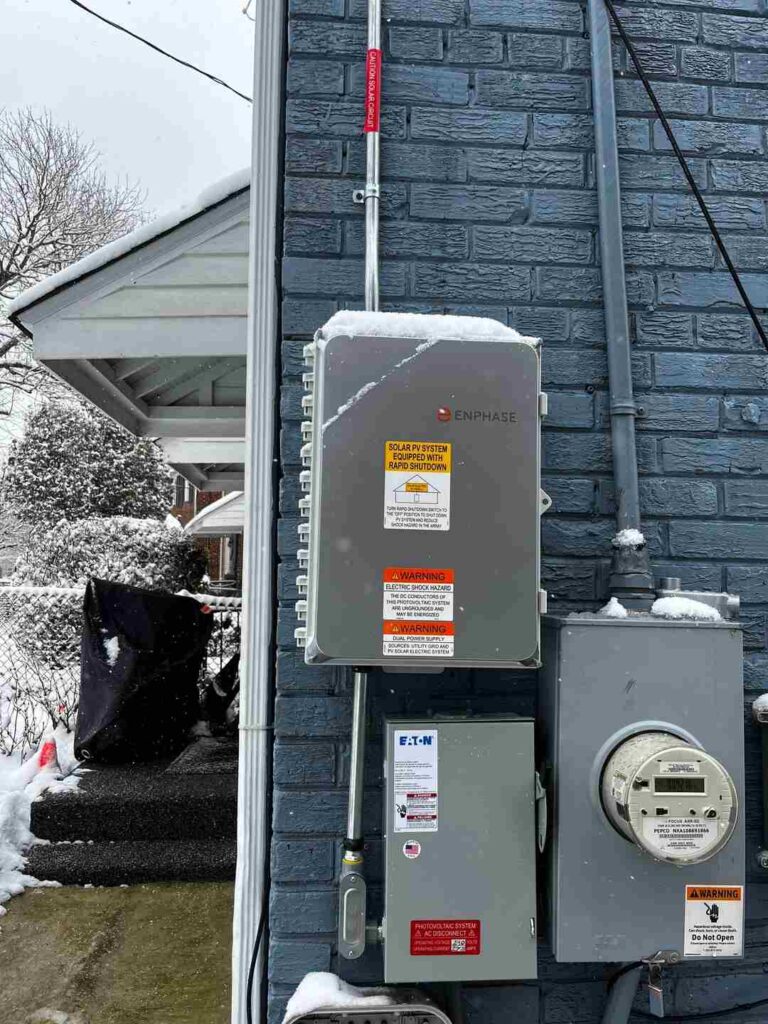 Solar equipment attached to a blue brick house in the snow.