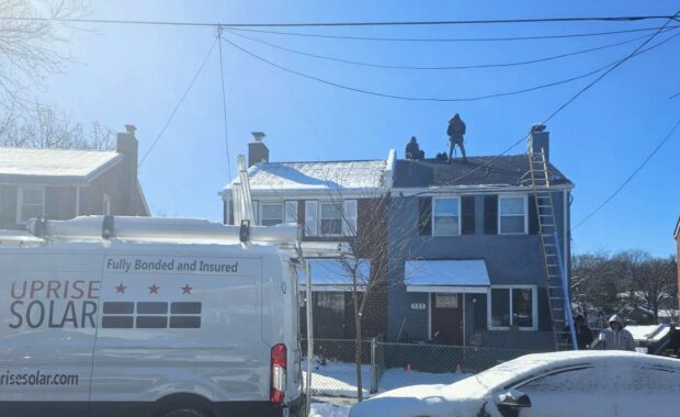 Uprise Solar installers work on a snowy day under a bright blue winter sky.