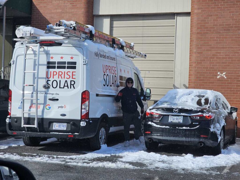 An Uprise installer flashes a thumbs up by the Uprise truck on a snowy day.